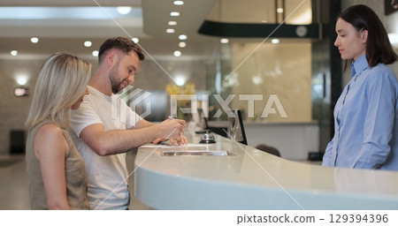 Man and woman walks up to desk and signs papers, takes keys and talks to female. Man signs papers, takes keys and talks to female manager. 129394396
