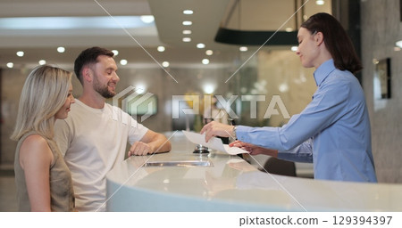 Man and woman walks up to desk and signs papers, takes keys and talks to female. Man signs papers, takes keys and talks to female manager. 129394397