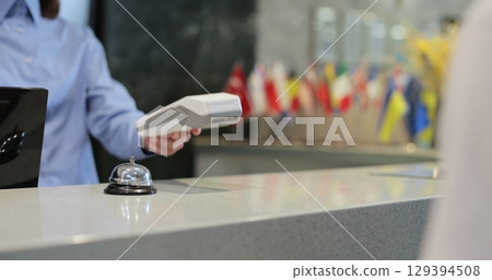 Customer with mobile phone pay for hotel reception, payment. Client, concierge service or people at help desk. Person at reception desk and doing check. Close up. 129394508