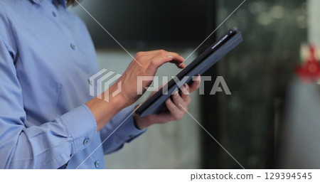 Close up of unrecognizable hotel worker wearing uniform standing in lobby or lounge using digital tablet. Woman manager in formalwear swiping on touch screen of digital tablet. 129394545