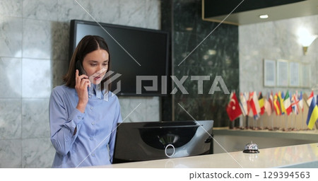 Woman phone call and smile at hotel reception for hospitality, friendly service. Receptionist of the hotel answering phone calls. Woman phone call and smile at hotel reception for hospitality, friendly service. Receptionist of the hotel answering phone calls. 129394563