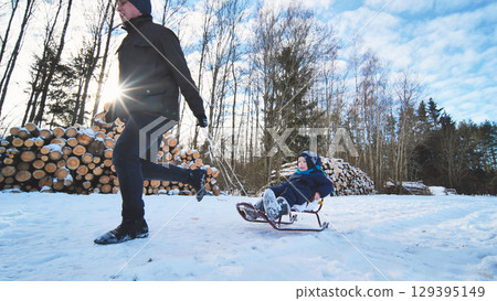Winter forest scene, father pulling sledding son, sharing playful moments amid snow covered trees and bright sunshine Winter forest scene, father pulling sledding son, sharing playful moments amid snow covered trees and bright sunshine 129395149