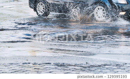 High speed vehicle splashing water while driving through roadside puddle, generating dramatic spray pattern High speed vehicle splashing water while driving through roadside puddle, generating dramatic spray pattern 129395193