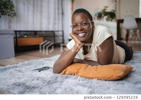 Young woman relaxing on carpet, smiling at camera Young woman relaxing on carpet, smiling at camera 129395219