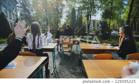 Teenage students are raising their hands to answer questions during an exam in an outdoor classroom setting 129395225