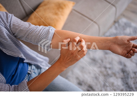 Woman scratching her itchy arm, suffering from dermatitis at home 129395229