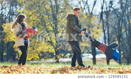 Happy family enjoying a sunny autumn day in a park, playing with their children among colorful fallen leaves 129395231