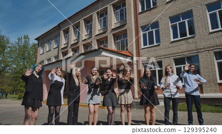 High school students happily waving in front of their school on a sunny day 129395240