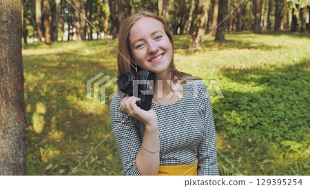 Young photographer smiling and holding a vintage camera in a green park during a sunny summer day Young photographer smiling and holding a vintage camera in a green park during a sunny summer day 129395254