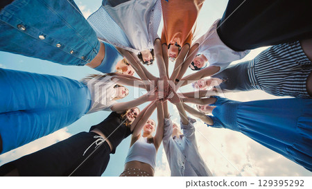 Group of cheerful school friends forming a circle and joining hands together against a blue sky, showcasing their unity and teamwork Group of cheerful school friends forming a circle and joining hands together against a blue sky, showcasing their unity and teamwork 129395292