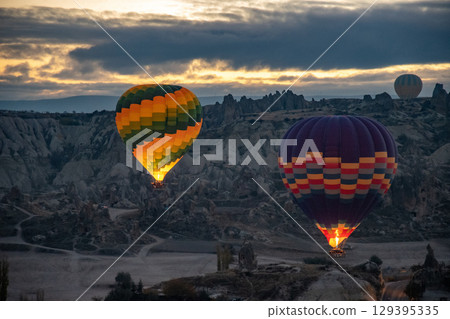 Colorful hot air balloons glowing in early morning dawn flying over mountain landscape Colorful hot air balloons glowing in early morning dawn flying over mountain landscape 129395335