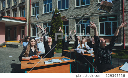 Cheerful students throwing books in the air to celebrate the end of the school year outside the school building Cheerful students throwing books in the air to celebrate the end of the school year outside the school building 129395336