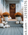 Cozy fall farmhouse porch with pumpkins, mums, and hay bales 129395576