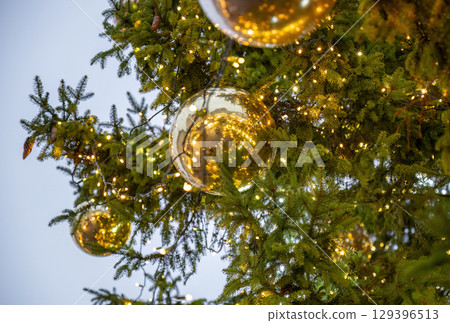 Close-up of Christmas tree branches with golden balls and festive lights Close-up of Christmas tree branches with golden balls and festive lights 129396513