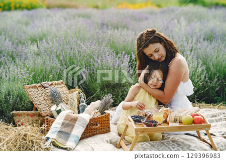 Mother with little daughter on lavender background. Beautiful woman and cute baby playing in meadow field. Family in a picnic. Mother with little daughter on lavender background. Beautiful woman and cute baby playing in meadow field. Family in a picnic. 129396983