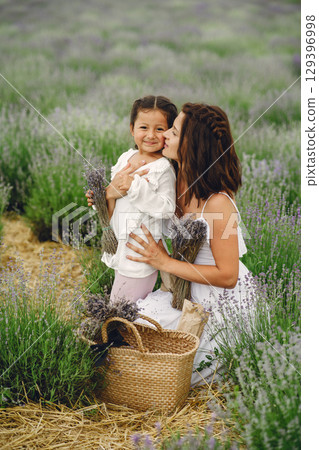 Mother with little daughter on lavender background. Beautiful woman and cute baby playing in meadow field. Family holiday in summer day. Mother with little daughter on lavender background. Beautiful woman and cute baby playing in meadow field. Family holiday in summer day. 129396998