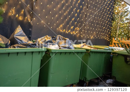 Green garbage bins with trash bags near Christmas tree and festive lights Green garbage bins with trash bags near Christmas tree and festive lights 129397120