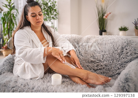 Young woman applying moisturizing cream on her legs at home 129397138