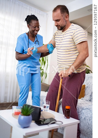 Nurse supports man with walking difficulties at home 129397167