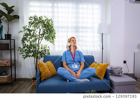 Young female doctor relaxing at home listening music with headphones Young female doctor relaxing at home listening music with headphones 129397193