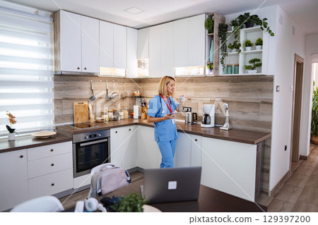 Female Doctor Drinking Tea and Using Smartphone in Kitchen during Work Break 129397200