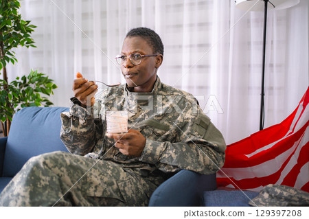 African american soldier eating yogurt at home with american flag 129397208