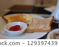 Female hand put Jam on Bread toast, glass of orange juice, sprigs spring tree with flowers, White Stone Background. Breakfast concept. Flat lay, top view. 129397439