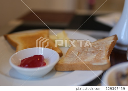 Female hand put Jam on Bread toast, glass of orange juice, sprigs spring tree with flowers, White Stone Background. Breakfast concept. Flat lay, top view. 129397439