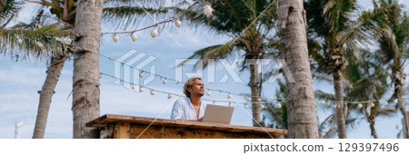 Solo traveler working on laptop at wooden desk under palm trees, enjoying freedom and inspiration in a serene outdoor setting Solo traveler working on laptop at wooden desk under palm trees, enjoying freedom and inspiration in a serene outdoor setting 129397496