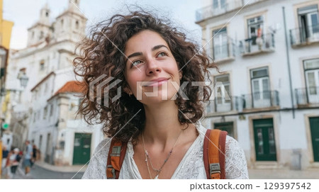 Solo female traveler with curly hair smiles while exploring vibrant city streets, embodying freedom and self-discovery in modern lifestyle adventure 129397542