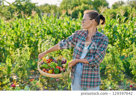 Portrait of woman showing basket with different fresh vegetables and herbs in garden Portrait of woman showing basket with different fresh vegetables and herbs in garden 129397642