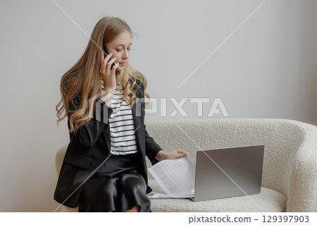 Businesswoman on phone call while reviewing documents at modern office workspace in the afternoon Businesswoman on phone call while reviewing documents at modern office workspace in the afternoon 129397903