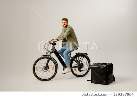 Delivery cyclist posing with bike and insulated bag in studio setting for promotional purposes 129397904