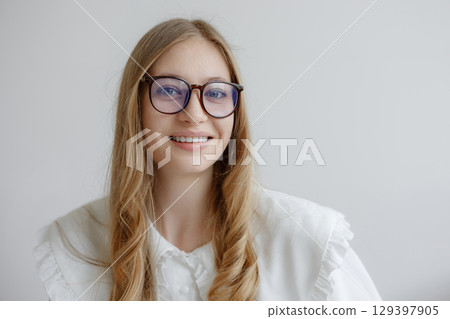 Smiling young woman with long hair and glasses in a light-filled studio setting Smiling young woman with long hair and glasses in a light-filled studio setting 129397905