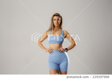 Fitness enthusiast poses confidently in light blue activewear in a minimalistic studio setting during daytime Fitness enthusiast poses confidently in light blue activewear in a minimalistic studio setting during daytime 129397906