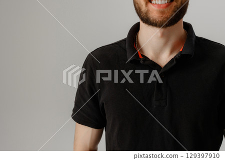 Smiling young man in black polo shirt against simple gray background during a casual indoor moment 129397910
