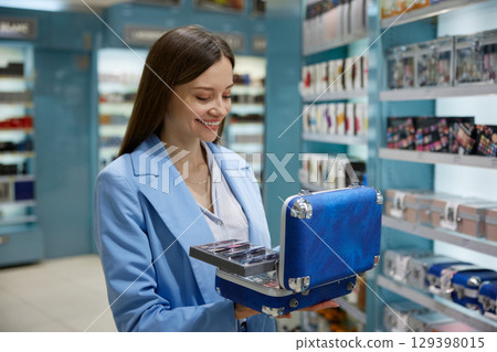 A woman is holding a blue suitcase while in a cosmetics store 129398015
