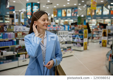 A woman in a blue jacket is closely examining makeup items 129398032
