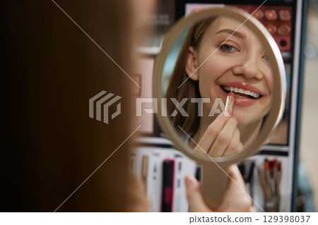 A woman is carefully applying bright lipstick while looking in a mirror 129398037