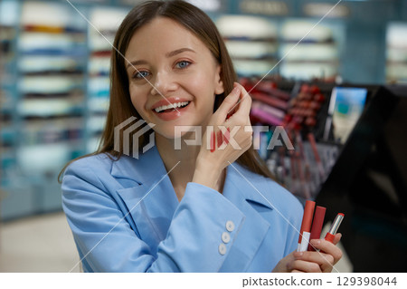Woman is carefully applying lipstick to her lips while in a store nearby Woman is carefully applying lipstick to her lips while in a store nearby 129398044