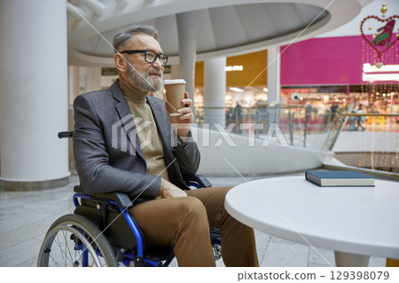 Stylish elderly man in a wheelchair happily enjoying a cup of coffee at a modern cafe Stylish elderly man in a wheelchair happily enjoying a cup of coffee at a modern cafe 129398079