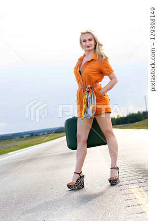 Blonde woman with a green retro suitcase standing on the highway. 129398149