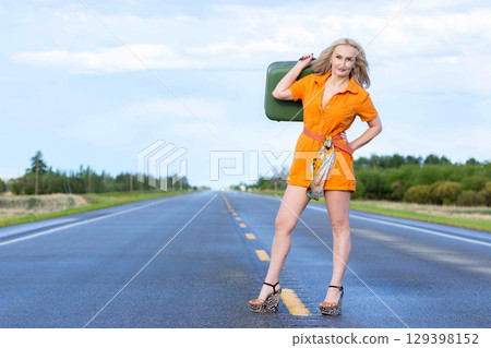 Blonde woman with a green retro suitcase standing on the highway. Blonde woman with a green retro suitcase standing on the highway. 129398152