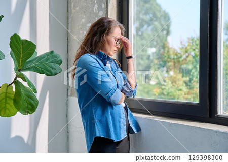 Mature tired, stressed woman standing at home near window 129398300