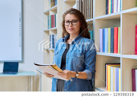 Portrait mature woman teacher, educational behavioral specialist with textbook in classroom 129398319