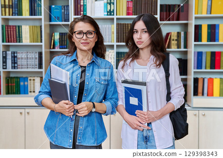Portrait of teenage girl student with female teacher mentor looking at camera in library 129398343