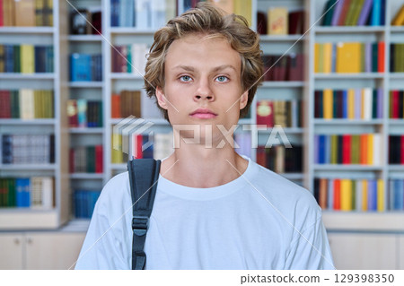 Headshot portrait of handsome serious teenage boy looking at camera in library 129398350