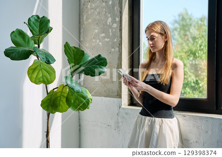 Portrait of serious young woman, profile view, with smartphone in home 129398374