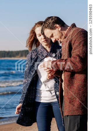 Loving couple walks on beach along sea on sunny autumn day. Weekend and lifestyle concept. Vertical photo. High quality photo Loving couple walks on beach along sea on sunny autumn day. Weekend and lifestyle concept. Vertical photo. High quality photo 129398463