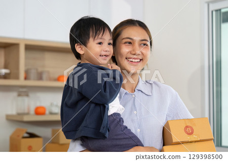 Family Business. A mother joyfully carries her child while managing packages. 129398500